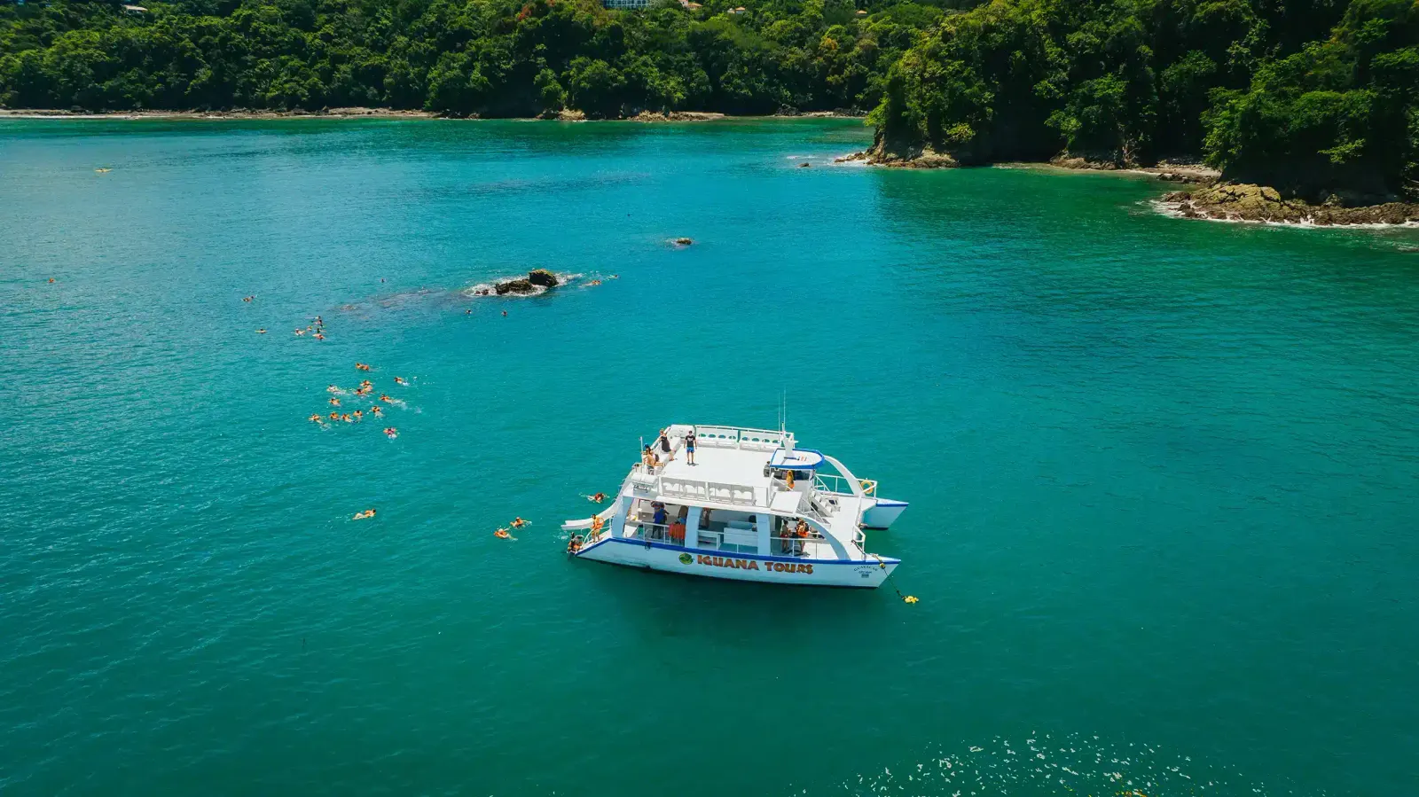 Vista aérea de un catamarán de tour anclado en una bahía turquesa con personas haciendo snorkel