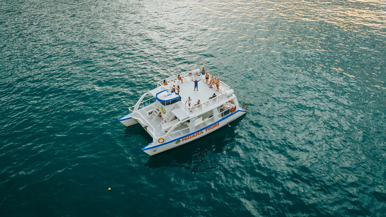 Vista aérea de invitados en la cubierta superior de un catamarán blanco en mar abierto