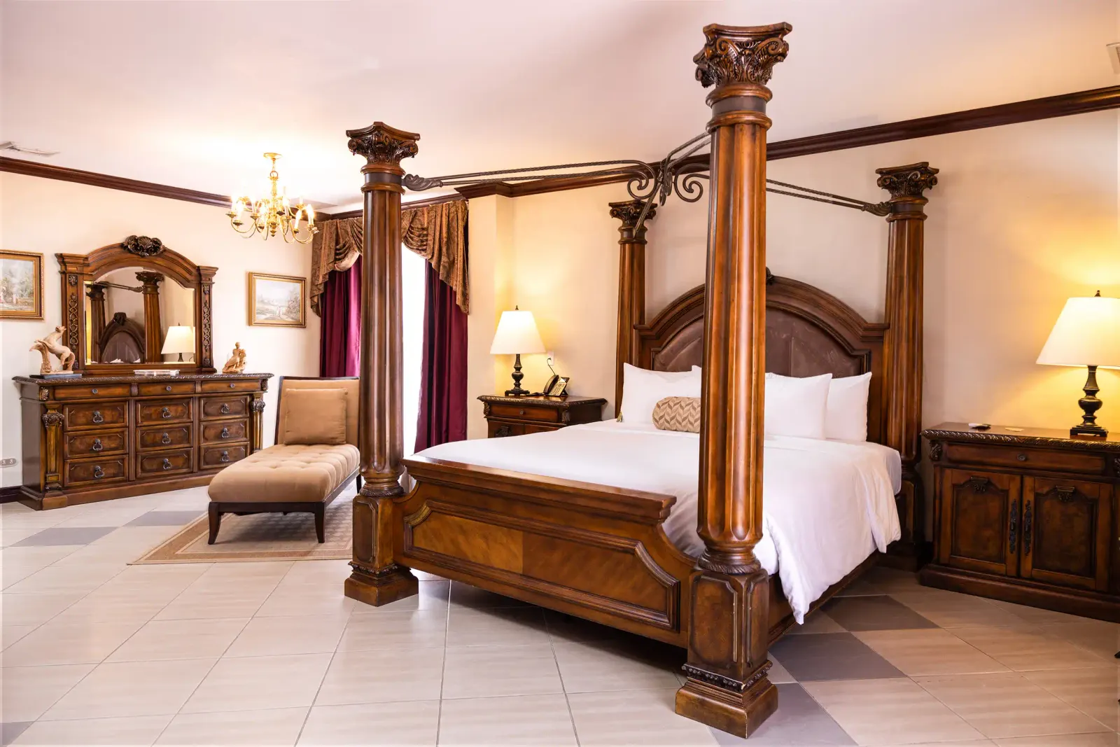 Family Suite bedroom with a carved four-poster king bed, a chaise longue and a dresser under a brass chandelier