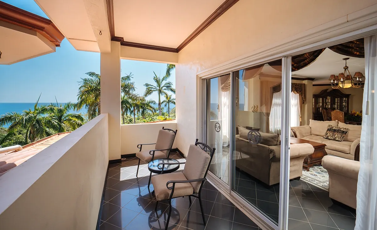 Family Suite terrace with chairs, looking over palms to the ocean, the living room through the glass doors