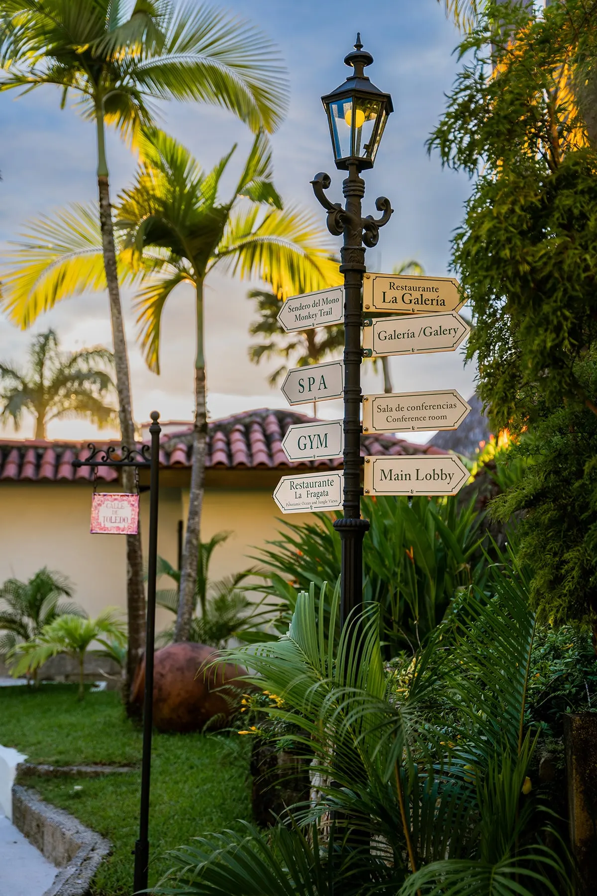Rótulos de madera en un poste de luz entre palmeras en los jardines de Parador