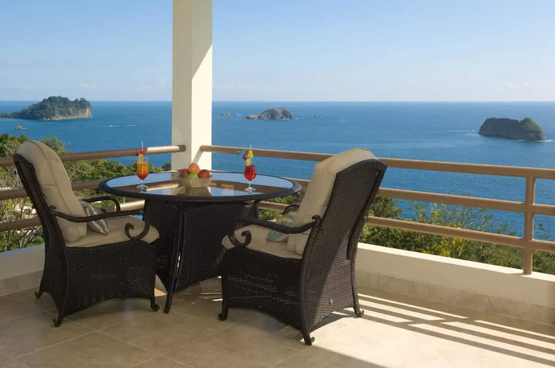 Dos sillones de mimbre y una mesa con cócteles en el balcón de una suite con vista al mar y a las islas
