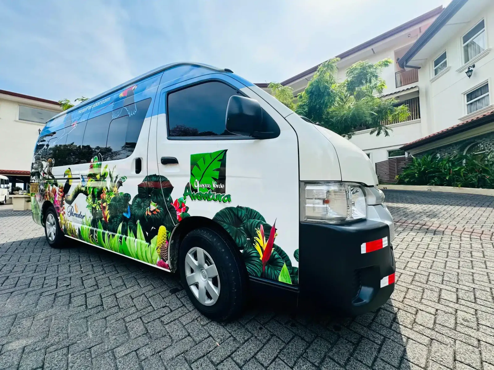 White Quepos Verde Aventura minivan painted with jungle leaves, parked on a paved drive