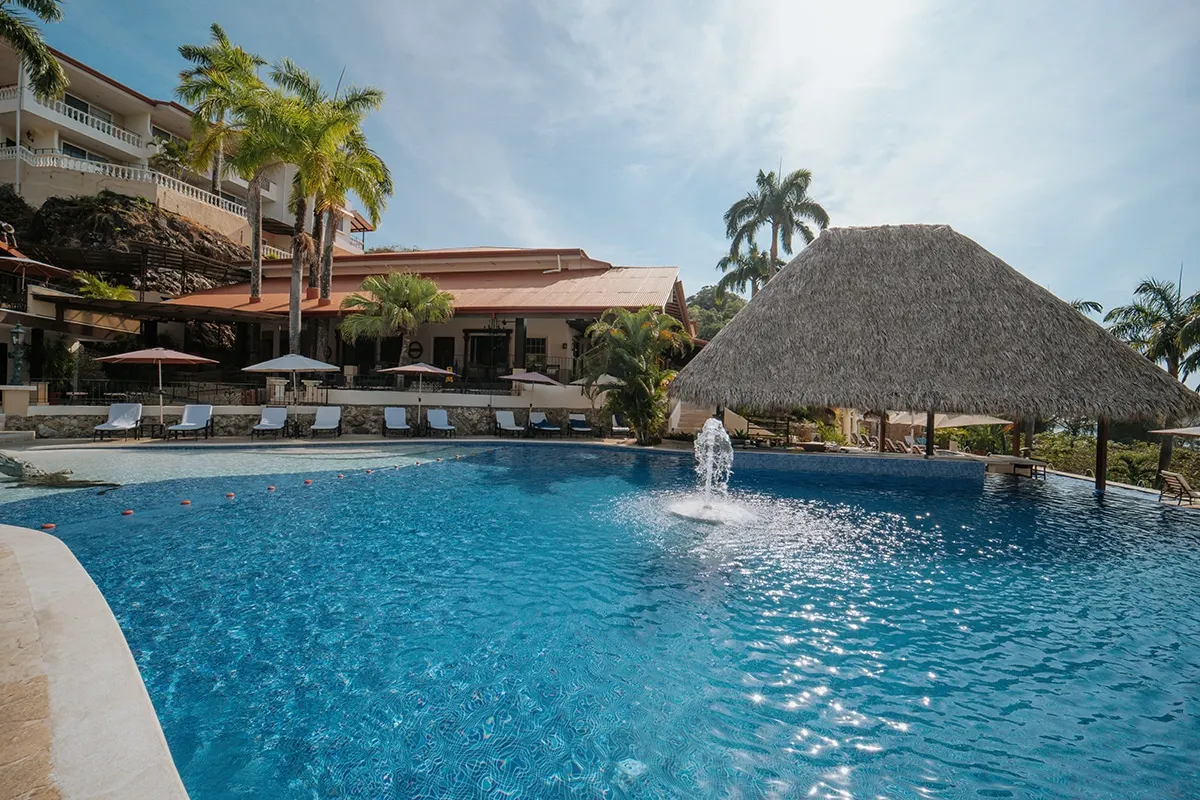 The main pool with its fountain, the thatched pool bar and palms under a blue sky