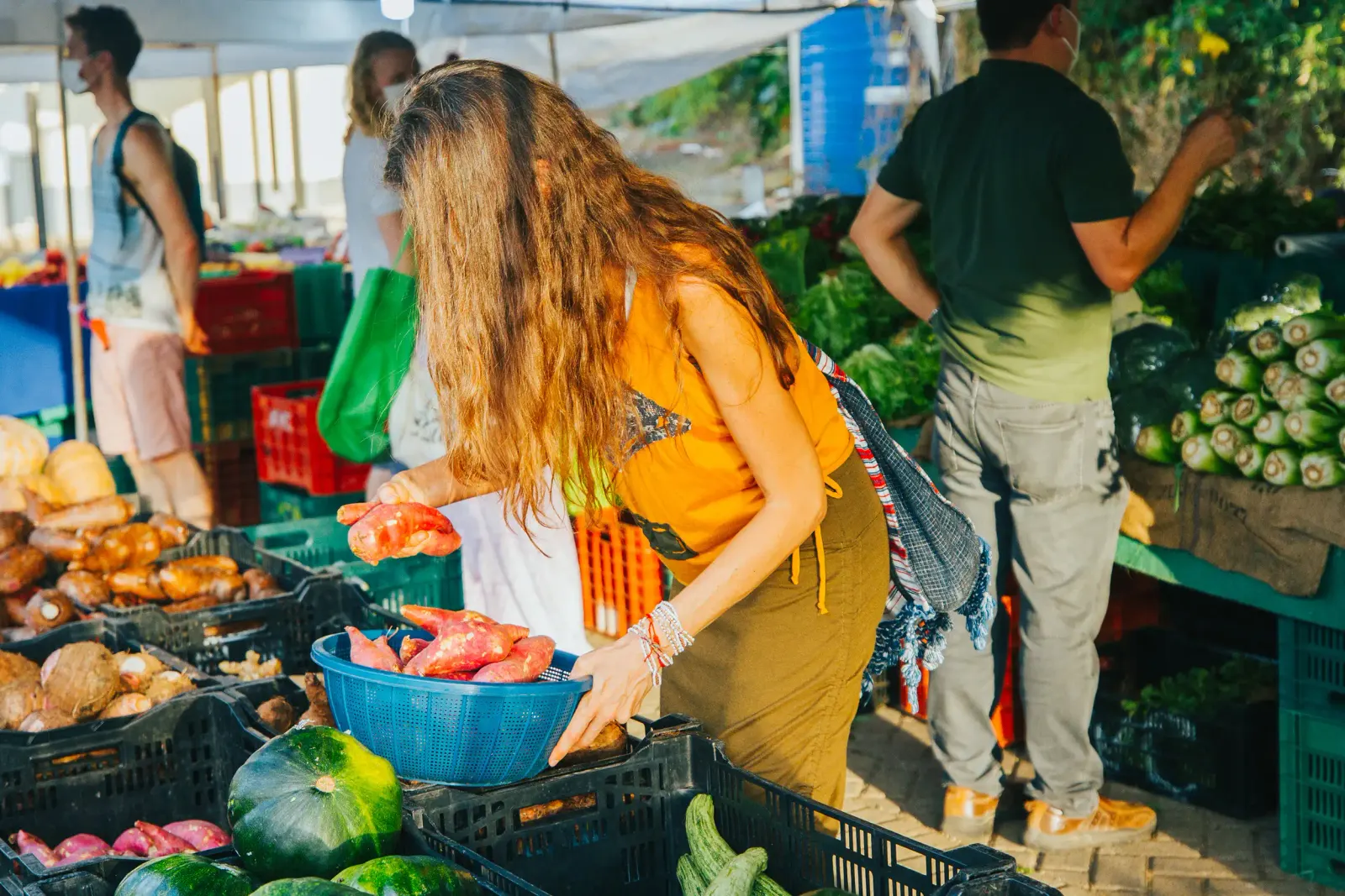 Clienta escogiendo camotes en un puesto de verduras de una feria al aire libre