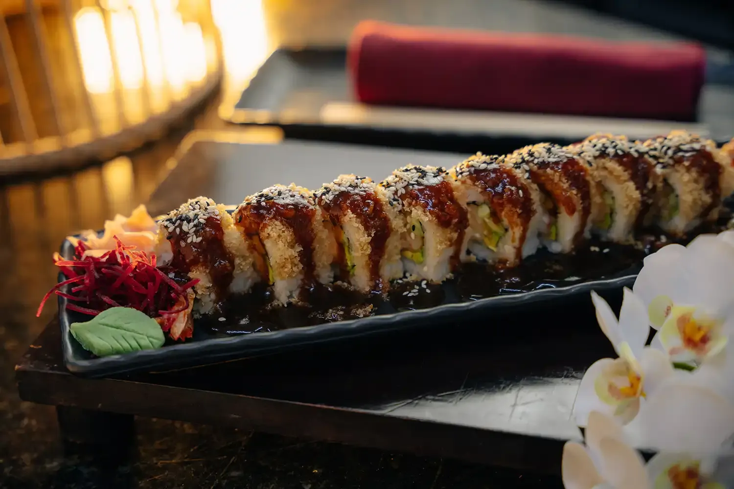 Un rollo de sushi con ajonjolí y salsa de anguila sobre un plato de pizarra negra