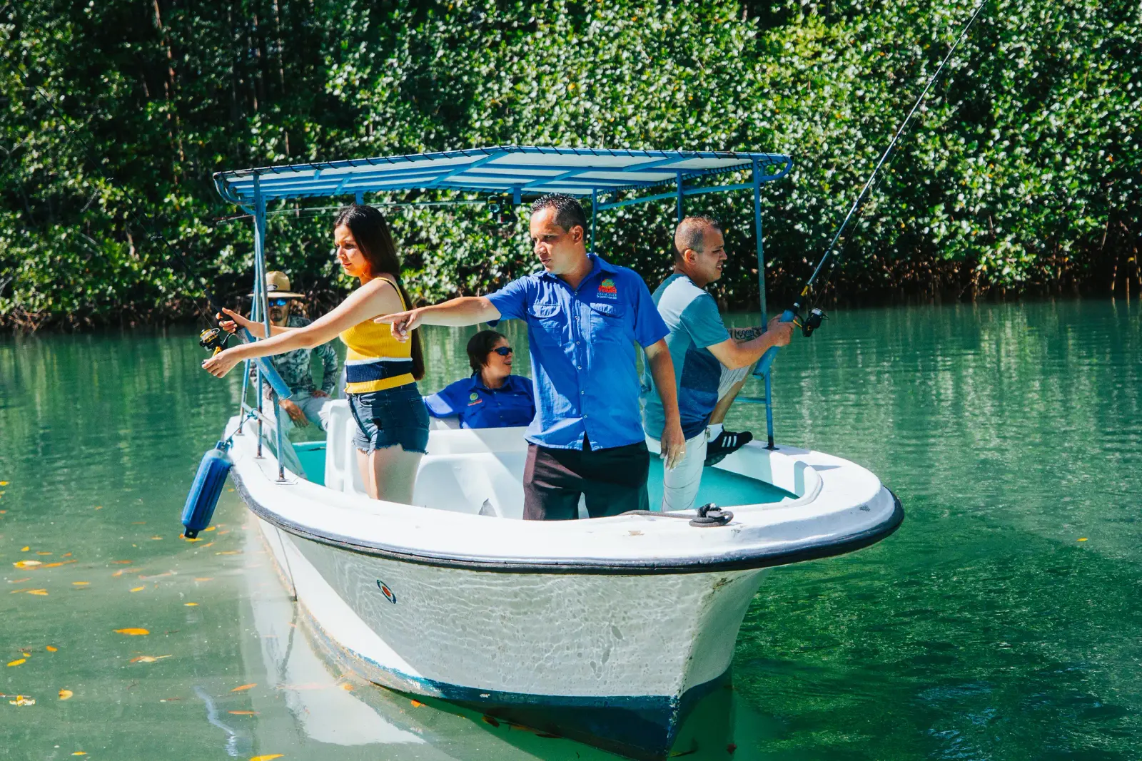 Guide and two guests casting from a small covered boat in a green mangrove channel