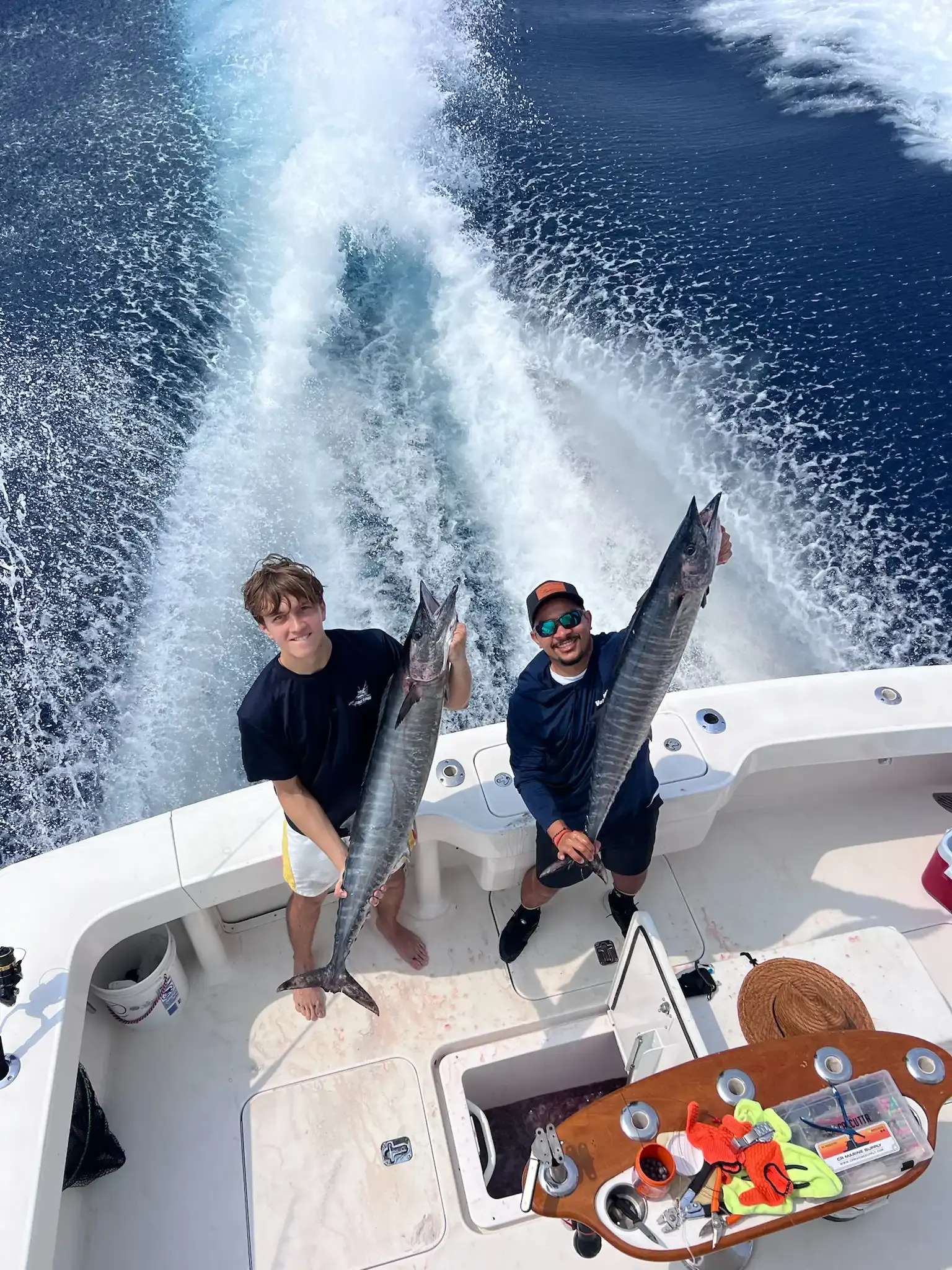 Two anglers on the Vuelto Loco deck each holding up a long silver fish