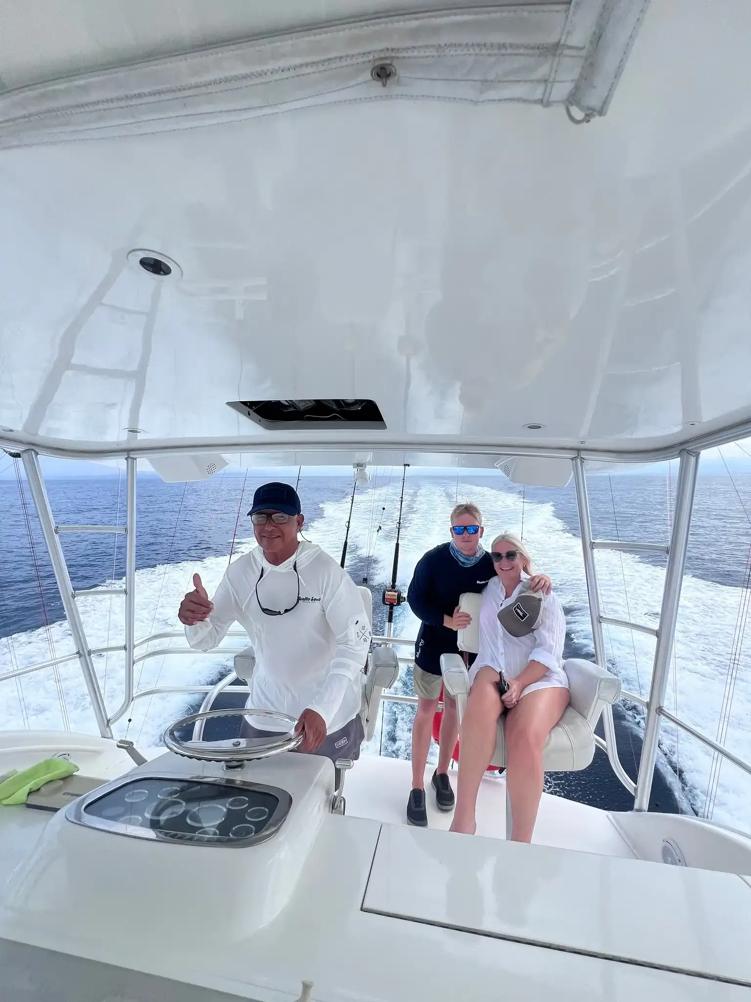 Captain at the helm on the Vuelto Loco flybridge with two guests giving a thumbs up