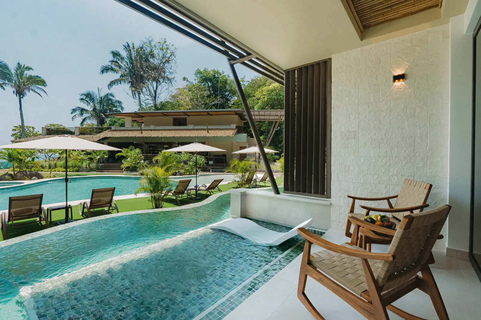 La piscina de inmersión curva junto a las Water Channel Suites de planta baja, con camastros y sombrillas al lado y palmeras al fondo