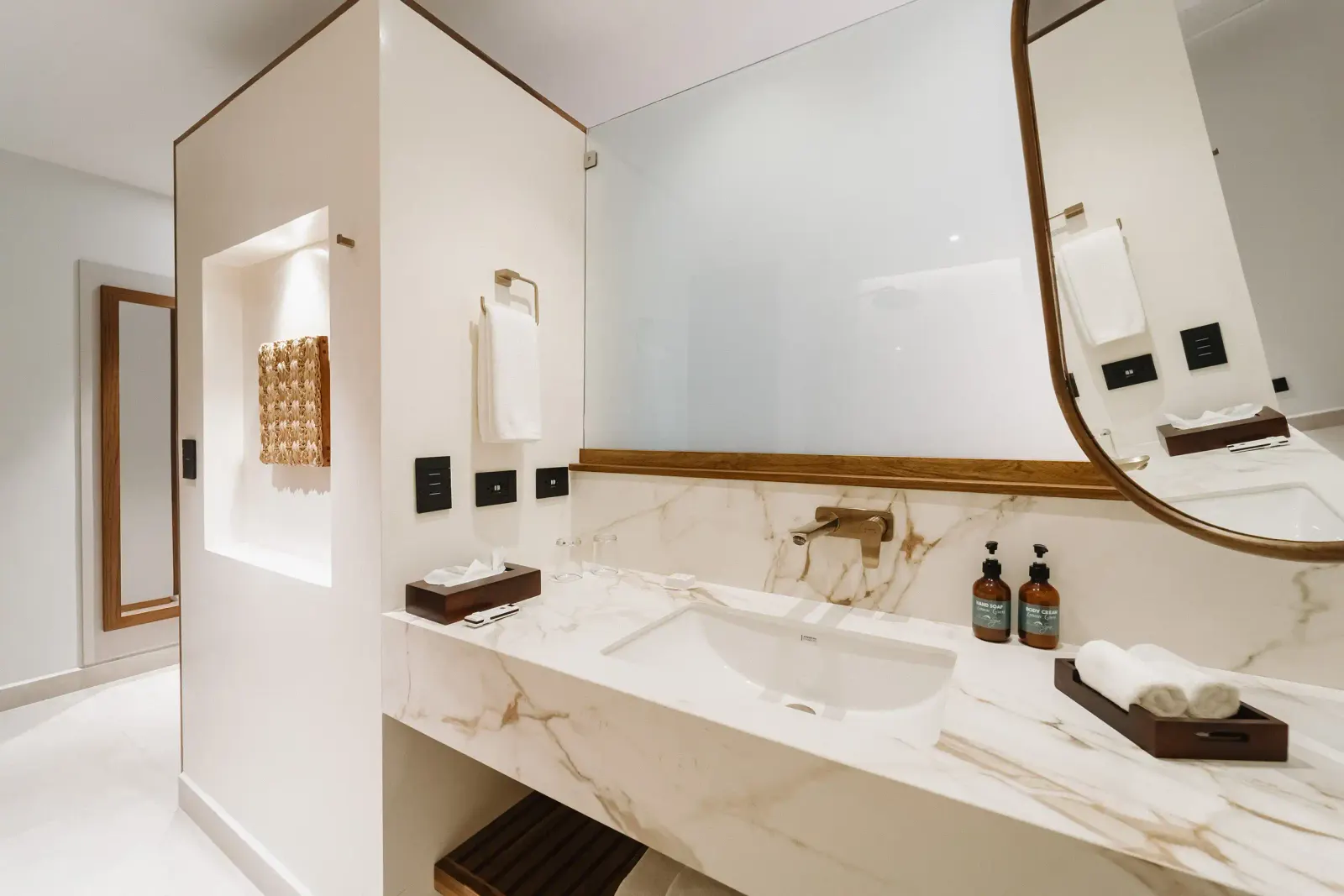 Mueble de baño blanco con sobre de mármol, espejo redondo, toalleros y detalles en madera café.