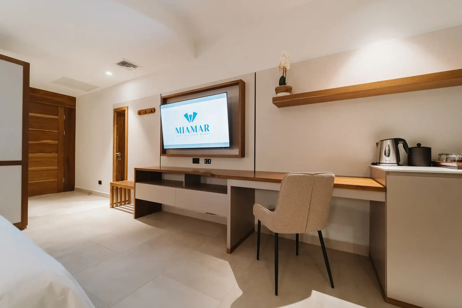 Sala de la suite con un televisor en la pared que muestra el logo de Miamar, un escritorio de madera y una silla beige.