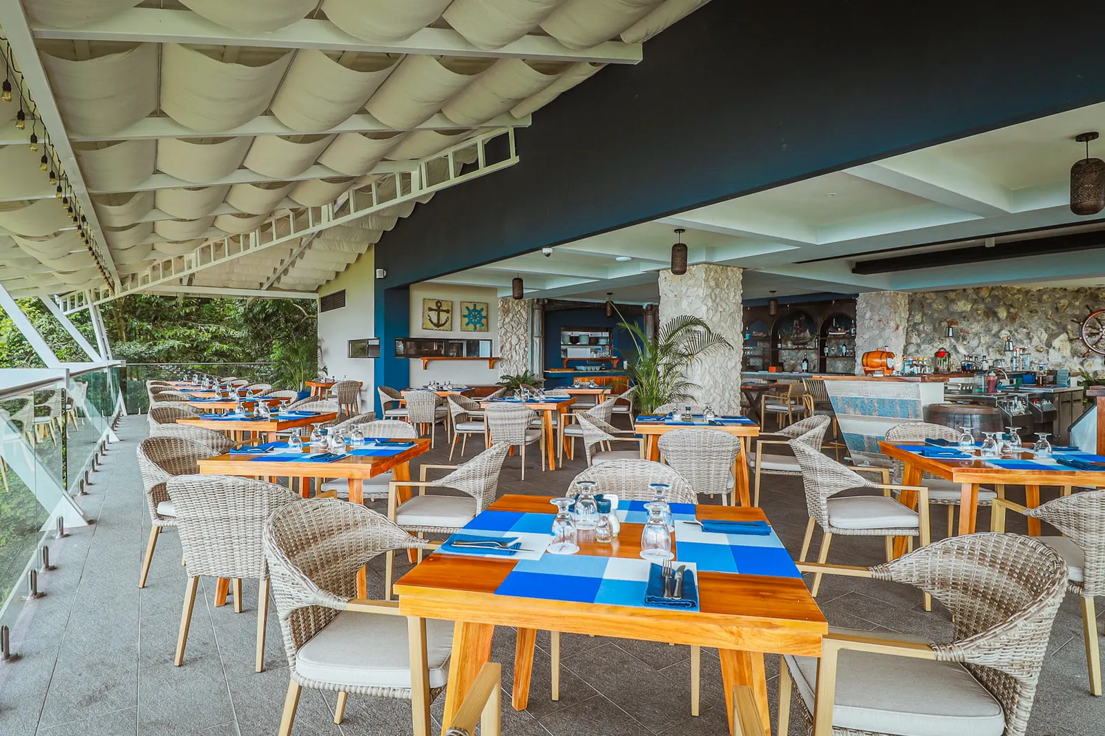 Rows of tables set with blue placemats under the fabric shades, the bar and a stone column at the back