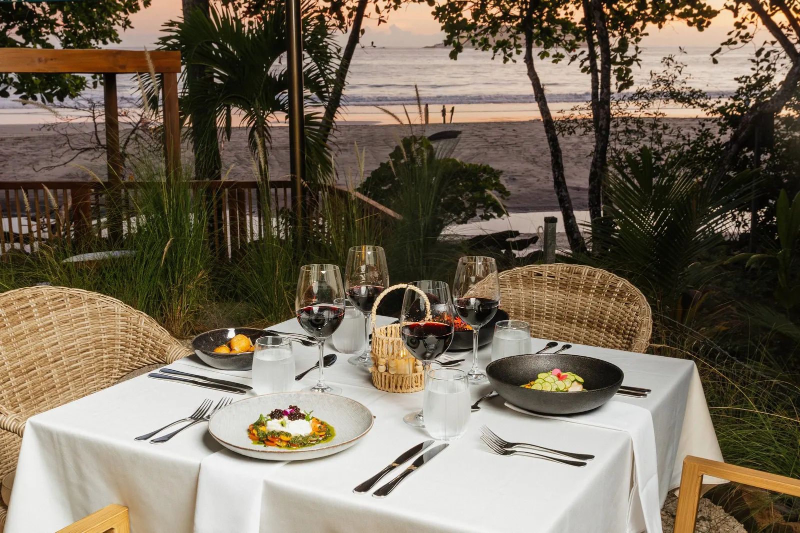 La terraza de Yemaya frente a la playa al atardecer, una mesa servida con copas de vino y platos, y Playa Espadilla entre las palmeras