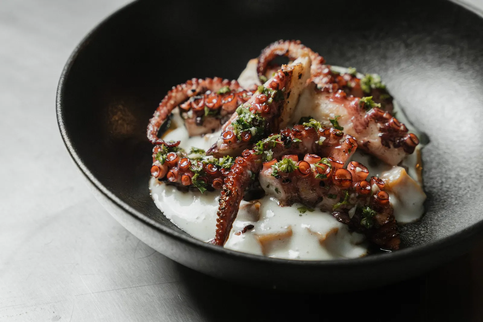 Pulpo a la parrilla sobre una salsa cremosa con hierbas frescas, un plato de Yemaya