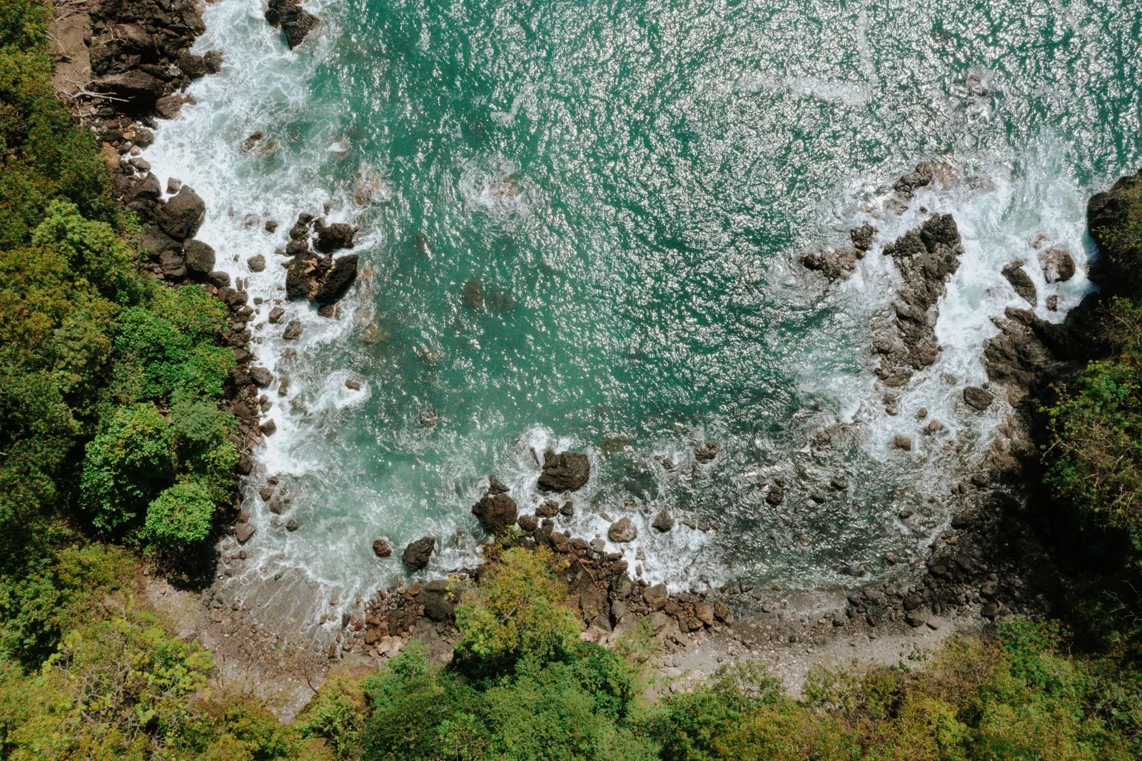 Vista aérea de una costa rocosa del Pacífico donde las olas turquesa revientan contra las rocas, bordeada por un bosque tropical denso
