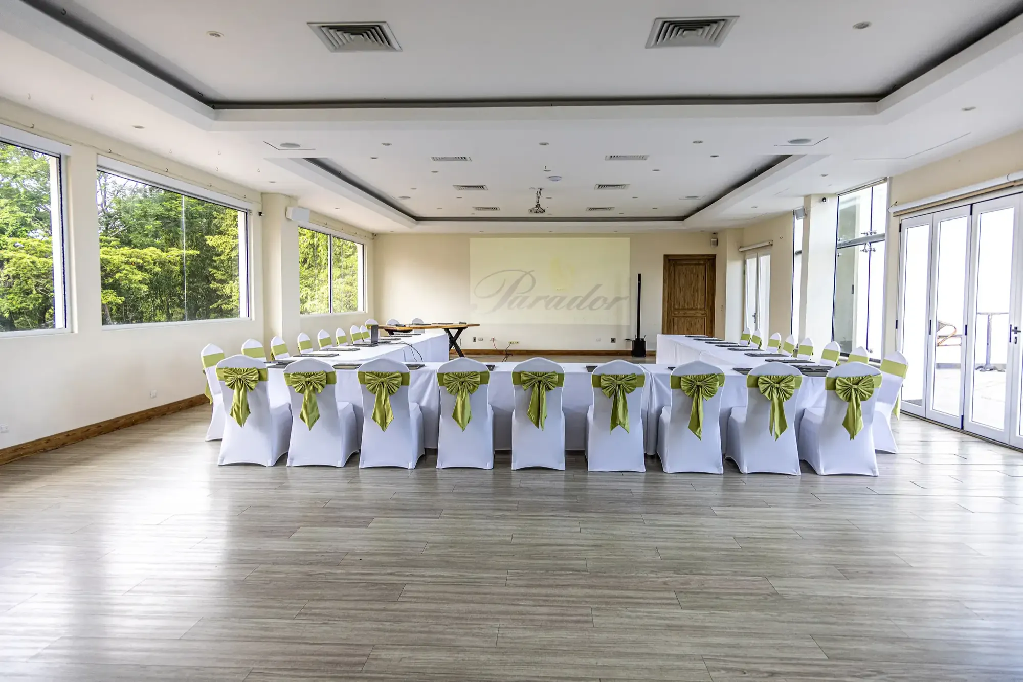 L'Orange Room set U-shape for a corporate meeting, chairs with sage sashes, a presentation live on the screen at the front of the room.