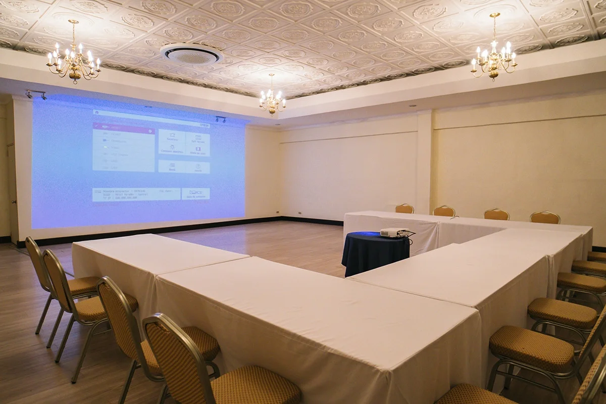 Close angle on El Rey Room's chandeliers and pressed-tin ceiling above a U-shaped meeting setup.