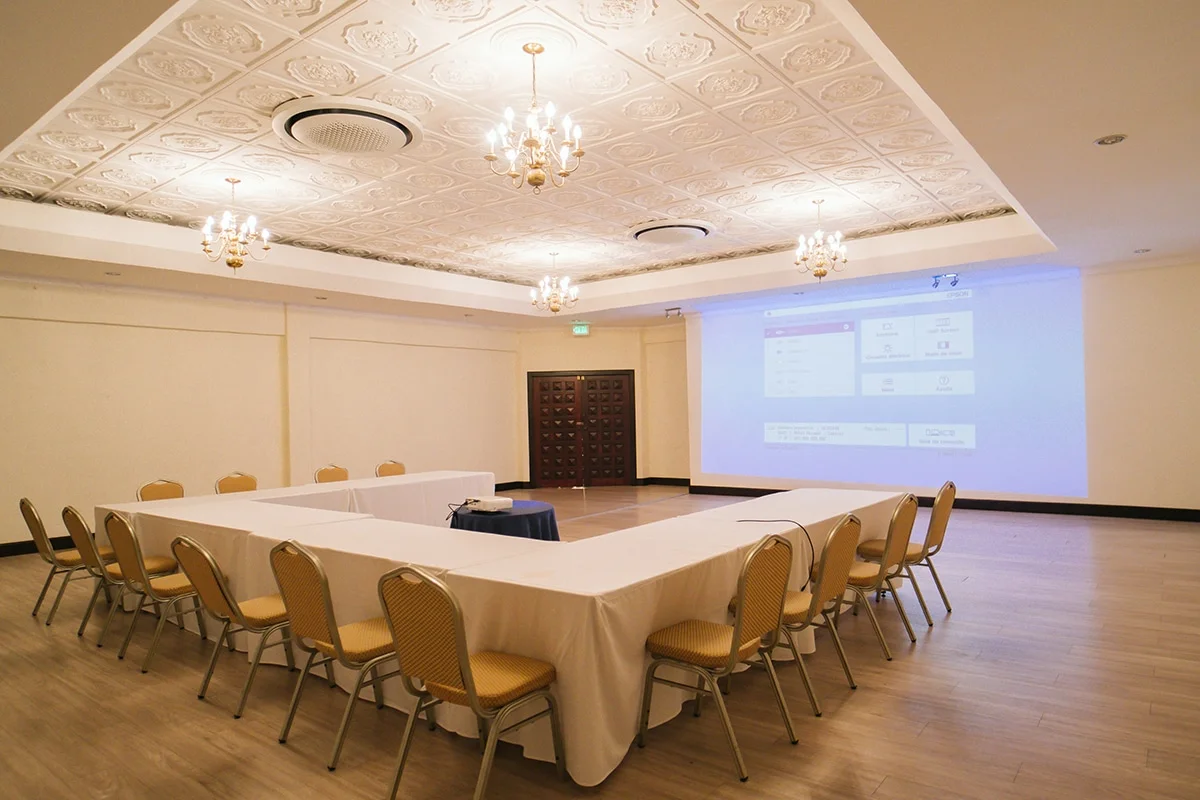 El Rey Room from the opposite angle, U-shaped seating facing a screen, the room's carved double doors visible at the back.