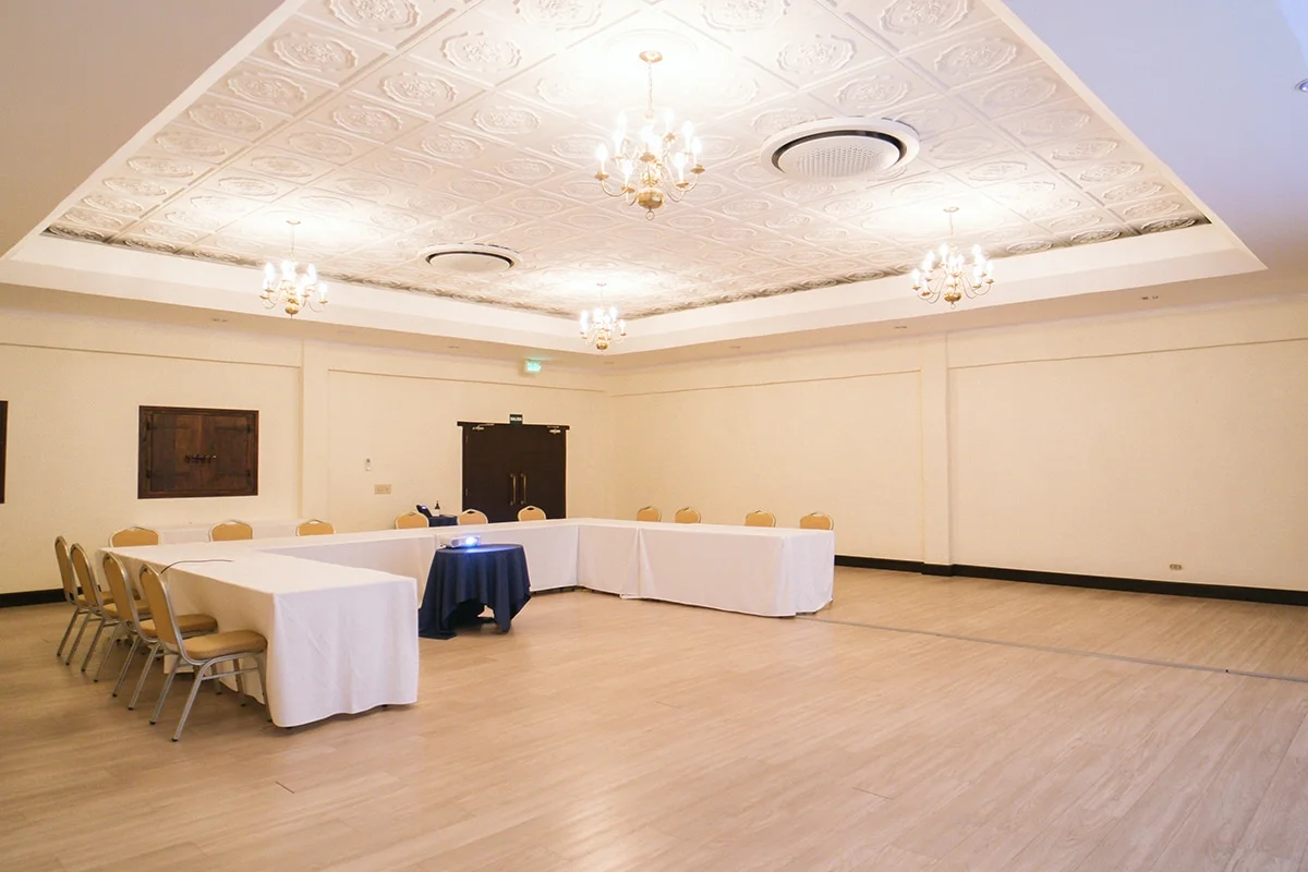 El Rey Room set U-shape for a meeting, ornate pressed-tin ceiling, three crystal chandeliers, dark wood doors at the far end.