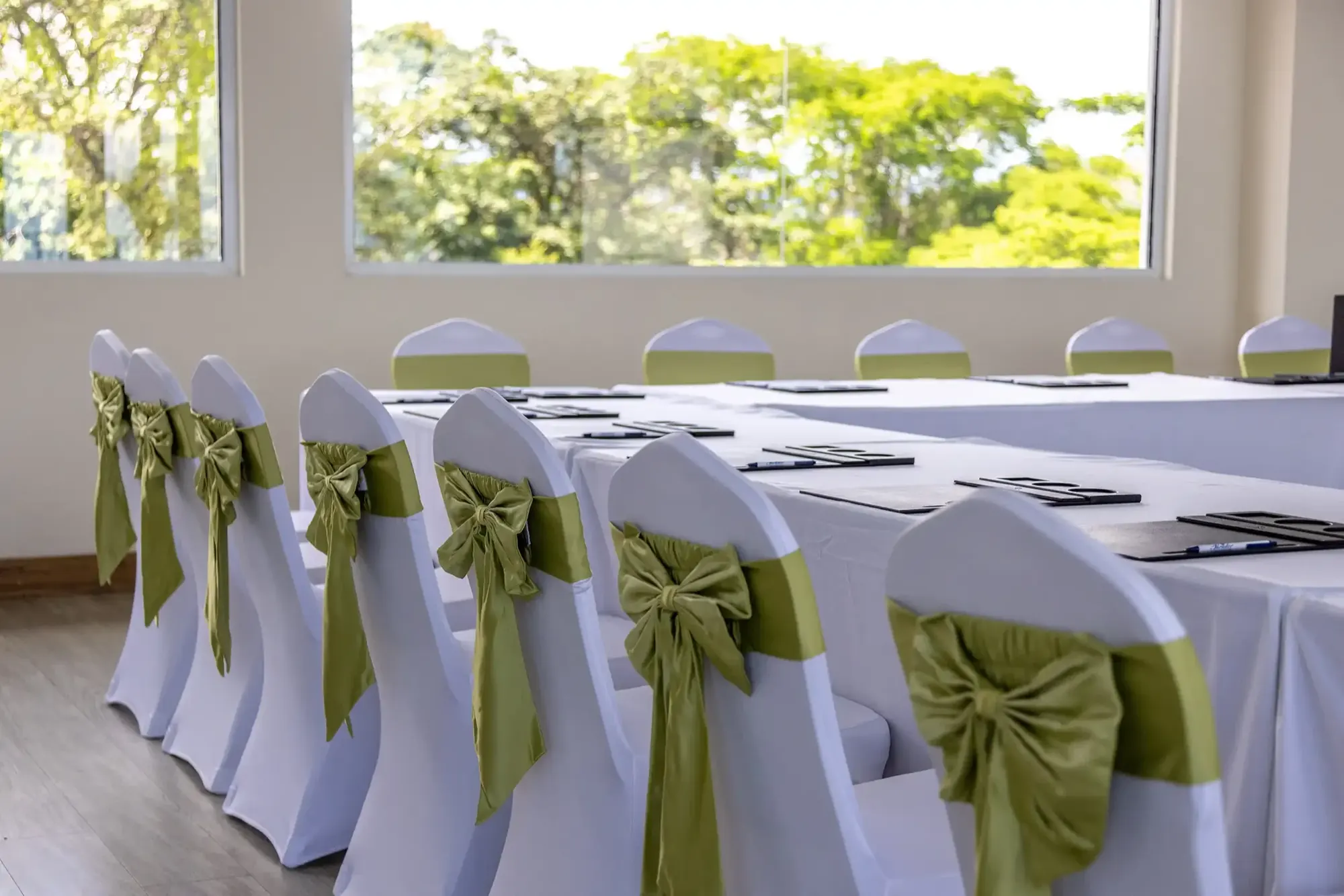 Close view of chairs with sage sashes lined up at a linen-covered table in L'Orange Room, forest visible through the windows.