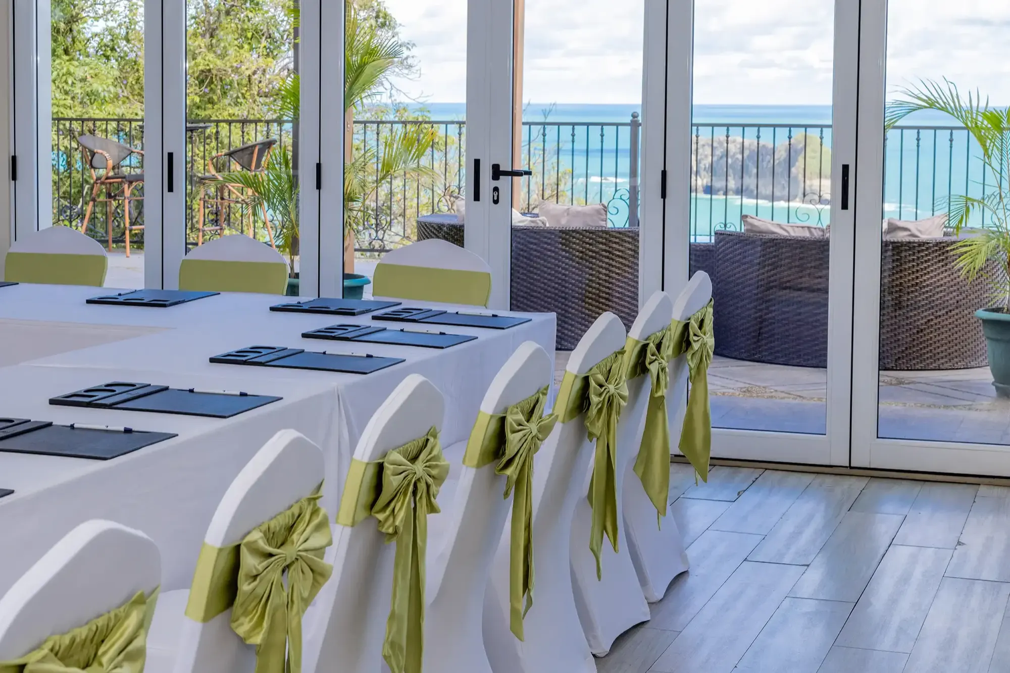 Boardroom table set for a meeting inside L'Orange Room with the folding glass doors open to the terrace and the Pacific beyond.