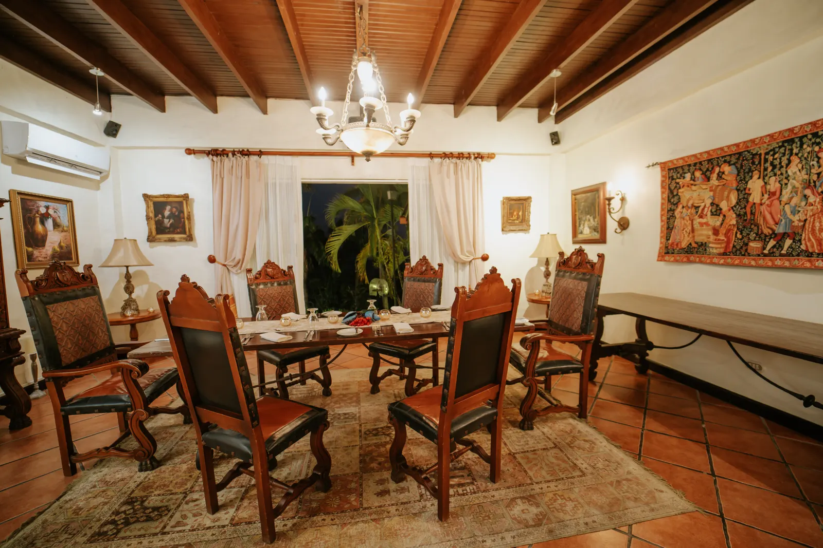 Elegante comedor privado en Parador Nature Resort con una mesa larga de madera, sillas de cuero tallado, lámpara de araña y tapices en las paredes