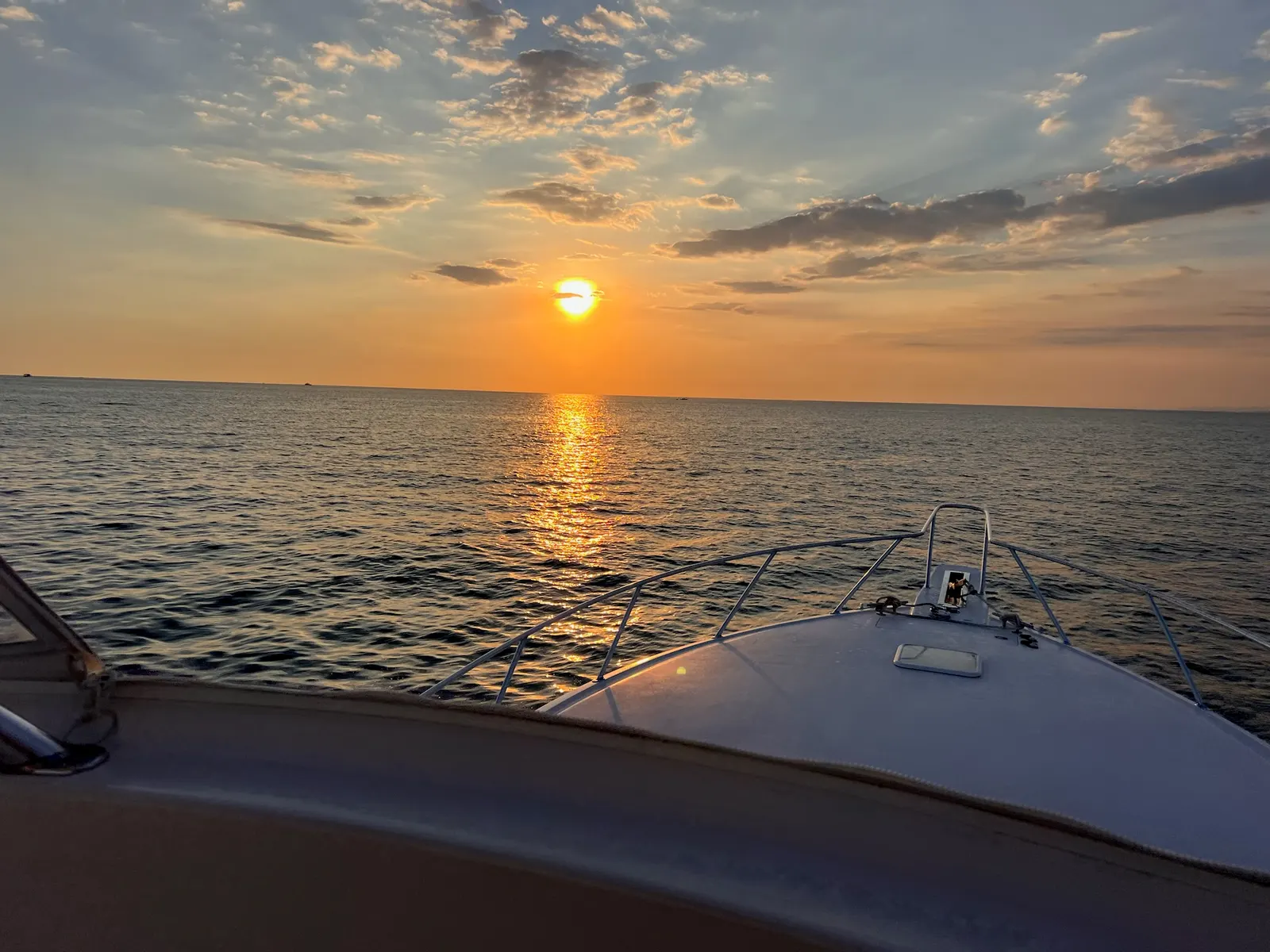 Atardecer visto desde la proa de un bote de pesca, con el sol bajo en el horizonte y un reflejo dorado sobre el océano Pacífico.