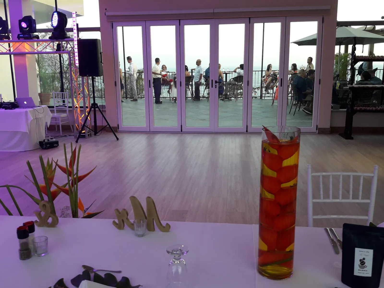 Salón de eventos de Parador Nature Resort montado para una recepción de boda, con pista de baile de madera, equipo de DJ y un centro de mesa con el monograma de madera de la pareja.