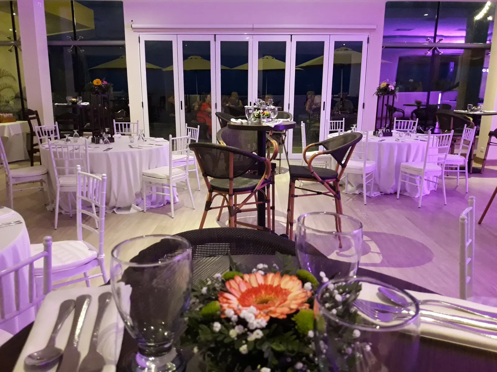 Ballroom set for an evening celebration, round tables with white linens and floral centerpieces under purple uplighting.