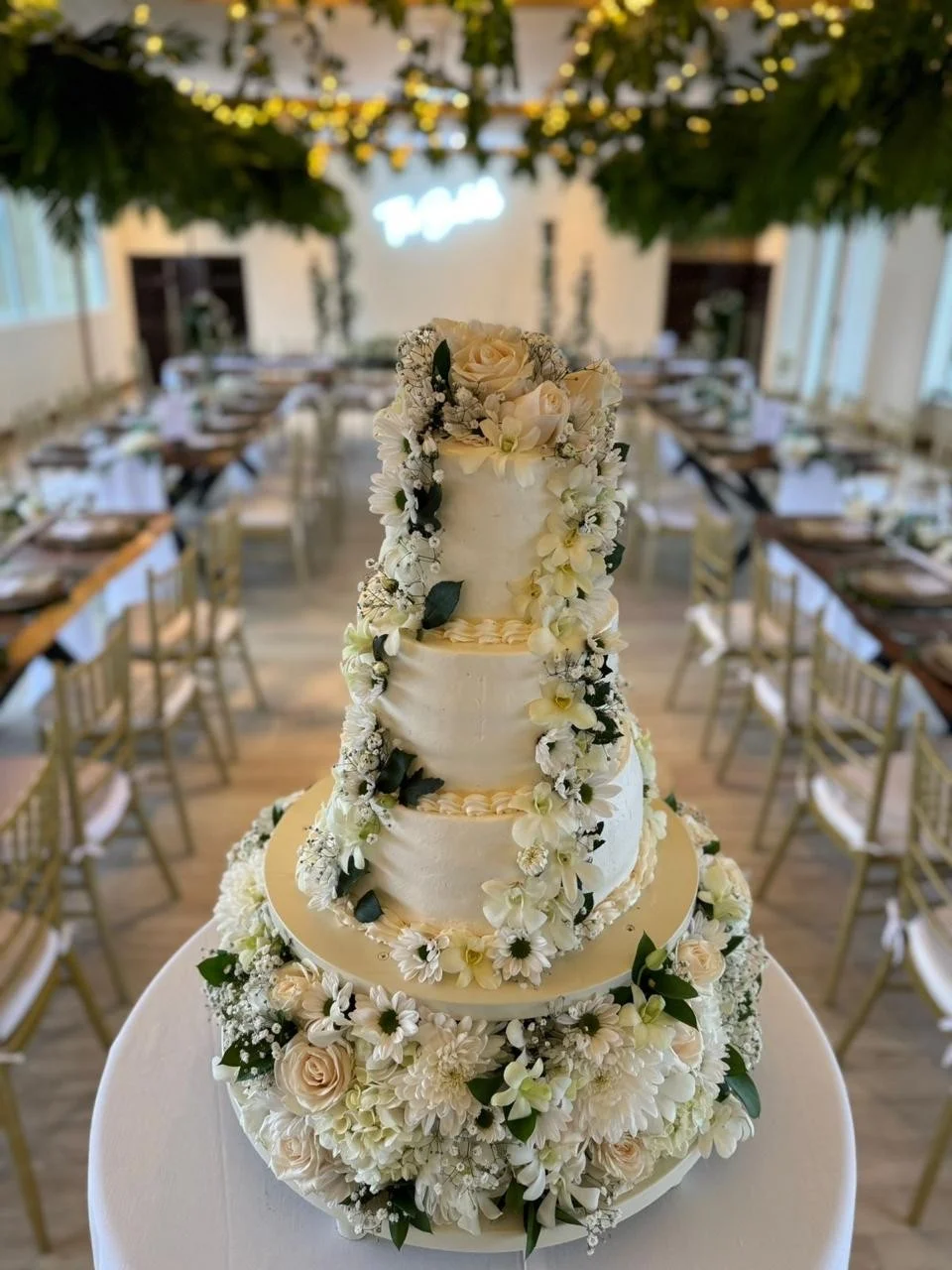Pastel de bodas alto de tres pisos, blanco, decorado con una cascada de rosas, margaritas y orquídeas.
