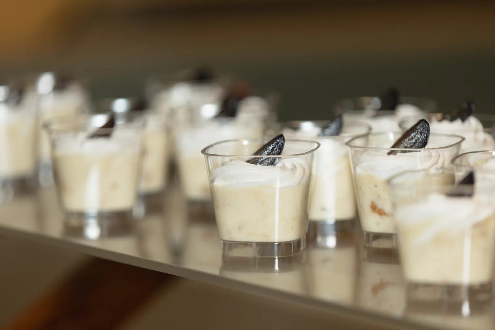 Filas de vasitos de flan de vainilla con crema batida y una teja de chocolate.