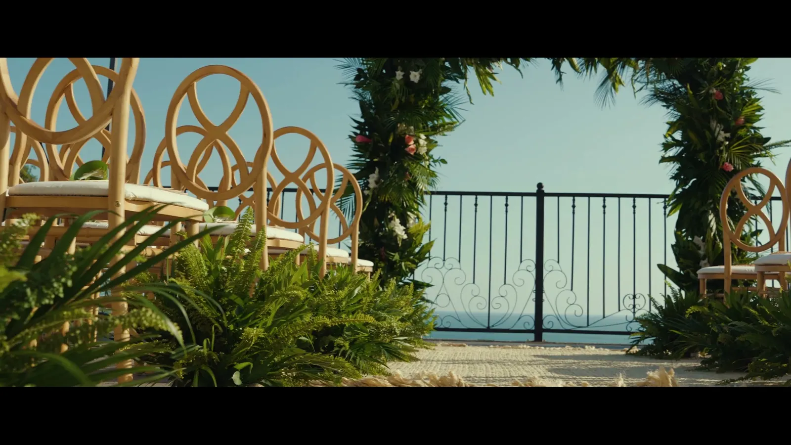 Fotograma del video de Parador: sillas de ratán y un arco floral sobre la terraza frente al mar, listos para una ceremonia.