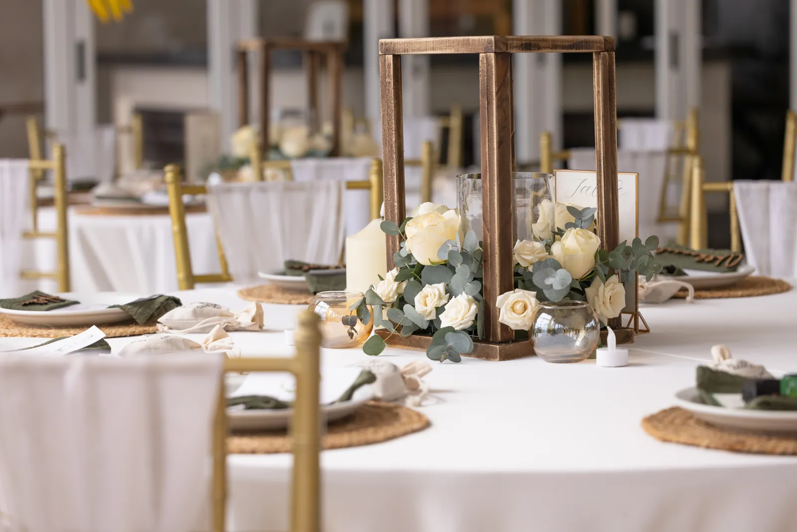 Mesa de recepción con un farol de madera como centro de mesa, rosas, eucalipto y sillas doradas.