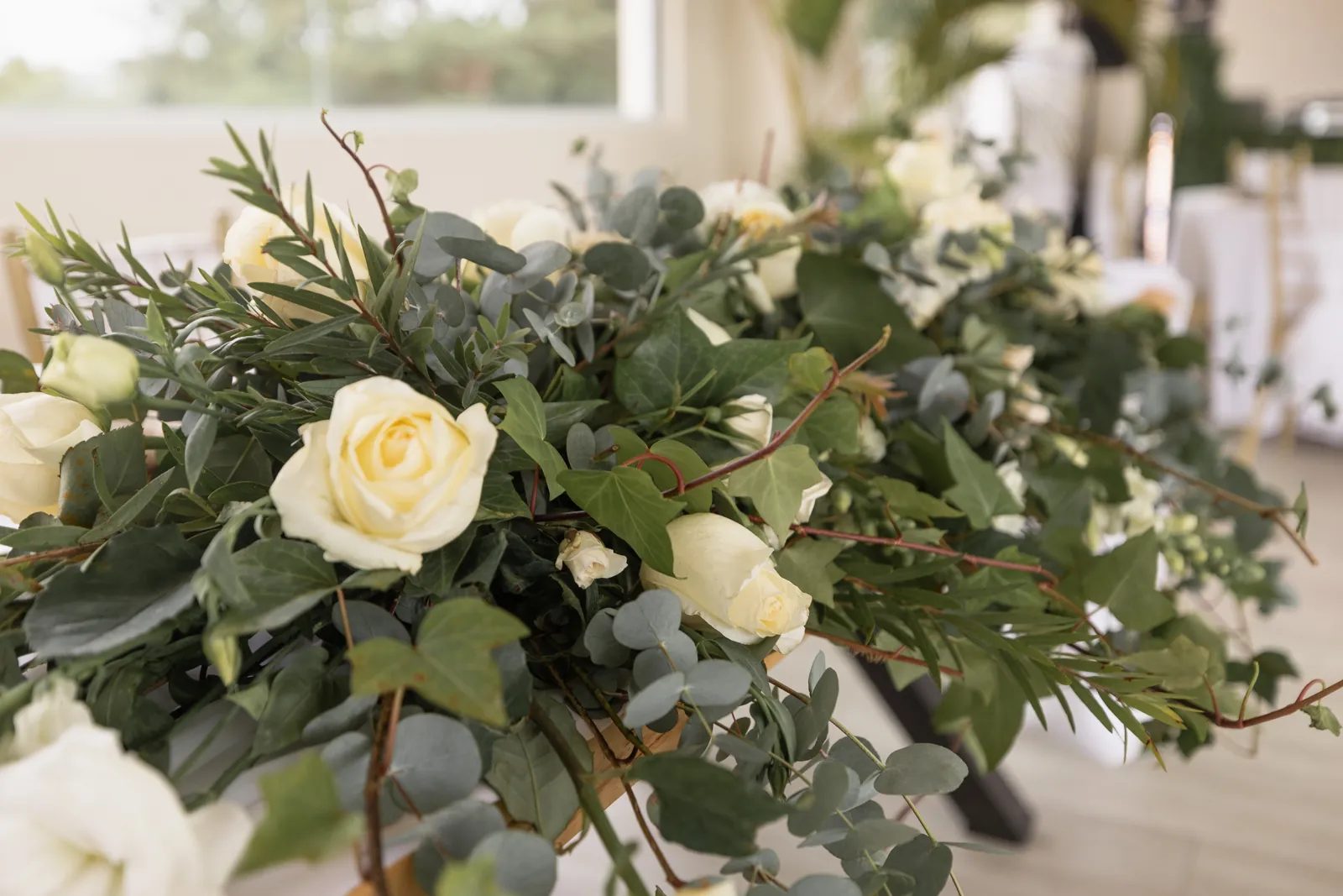 Guirnalda de rosas color crema y eucalipto a lo largo de una mesa de recepción.