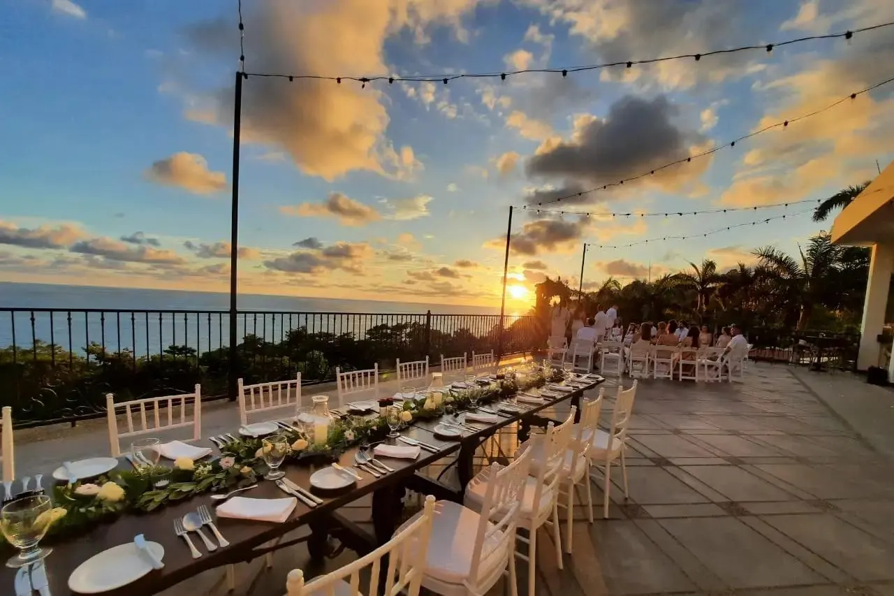 Cielo del atardecer sobre una mesa de recepción de boda con vista al océano, adornada con luces.