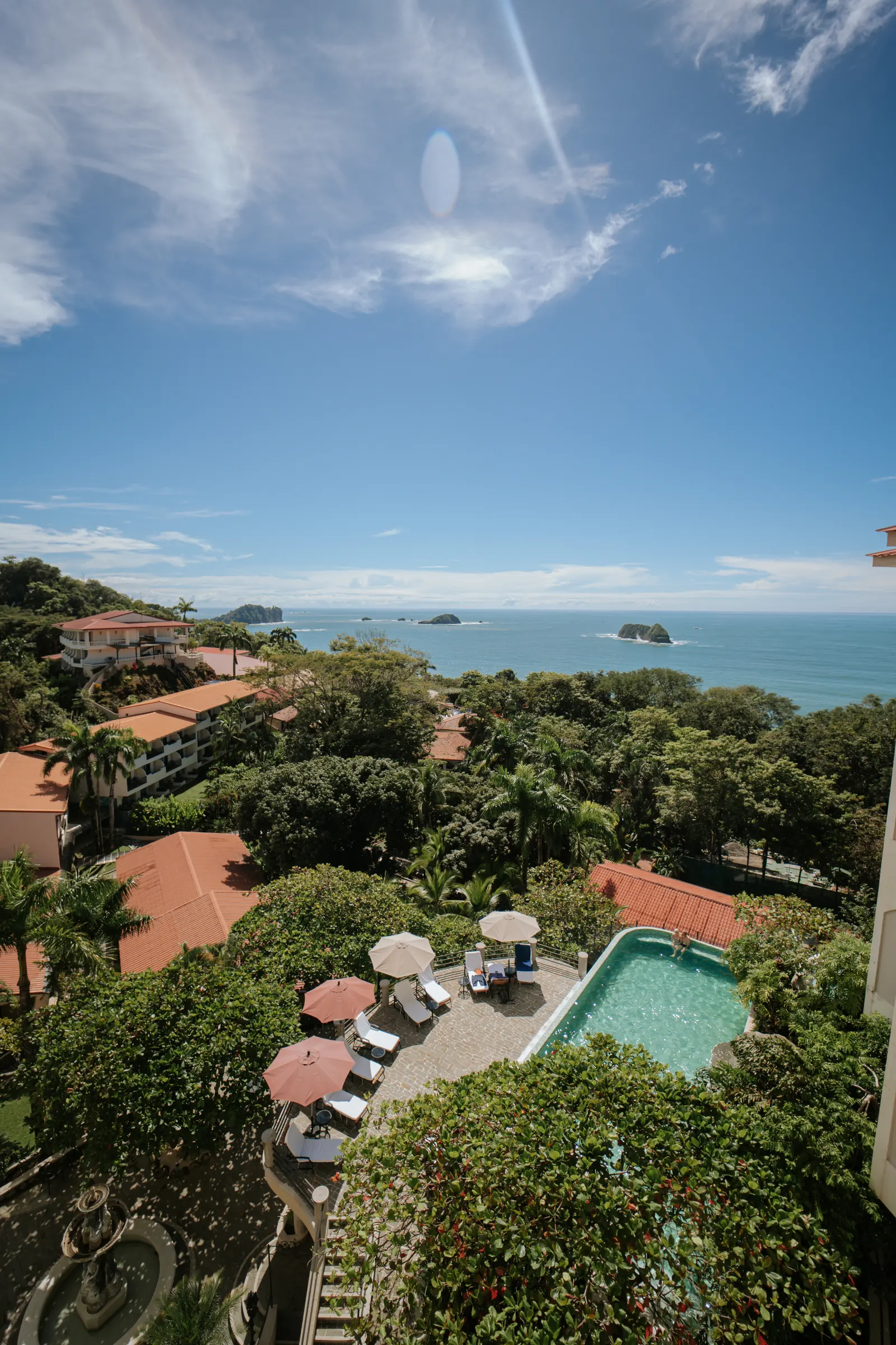Aerial view from a Parador Penthouse balcony over the pool deck, jungle canopy, and Pacific Ocean with rock islands.