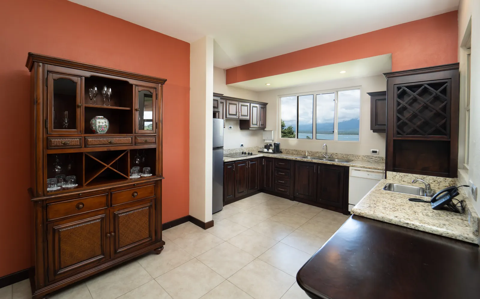 Penthouse kitchenette at Parador Nature Resort with dark wood cabinets, granite counters, wine rack, and an ocean view window over the sink