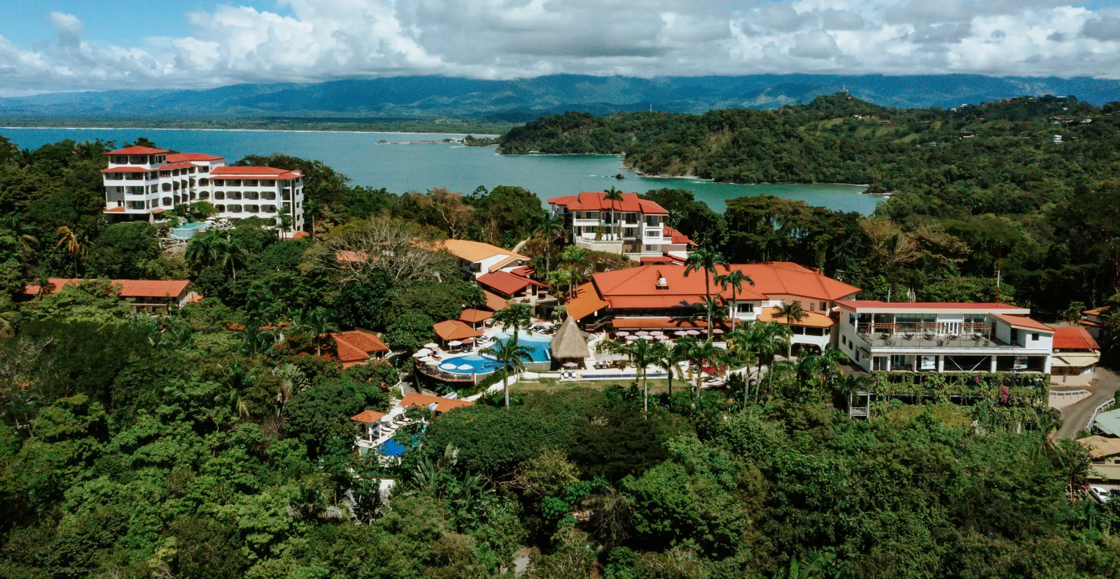 Aerial view of Parador Nature Resort & Spa on the Punta Quepos point, with the pools, red tile roofs and rainforest above the Pacific.