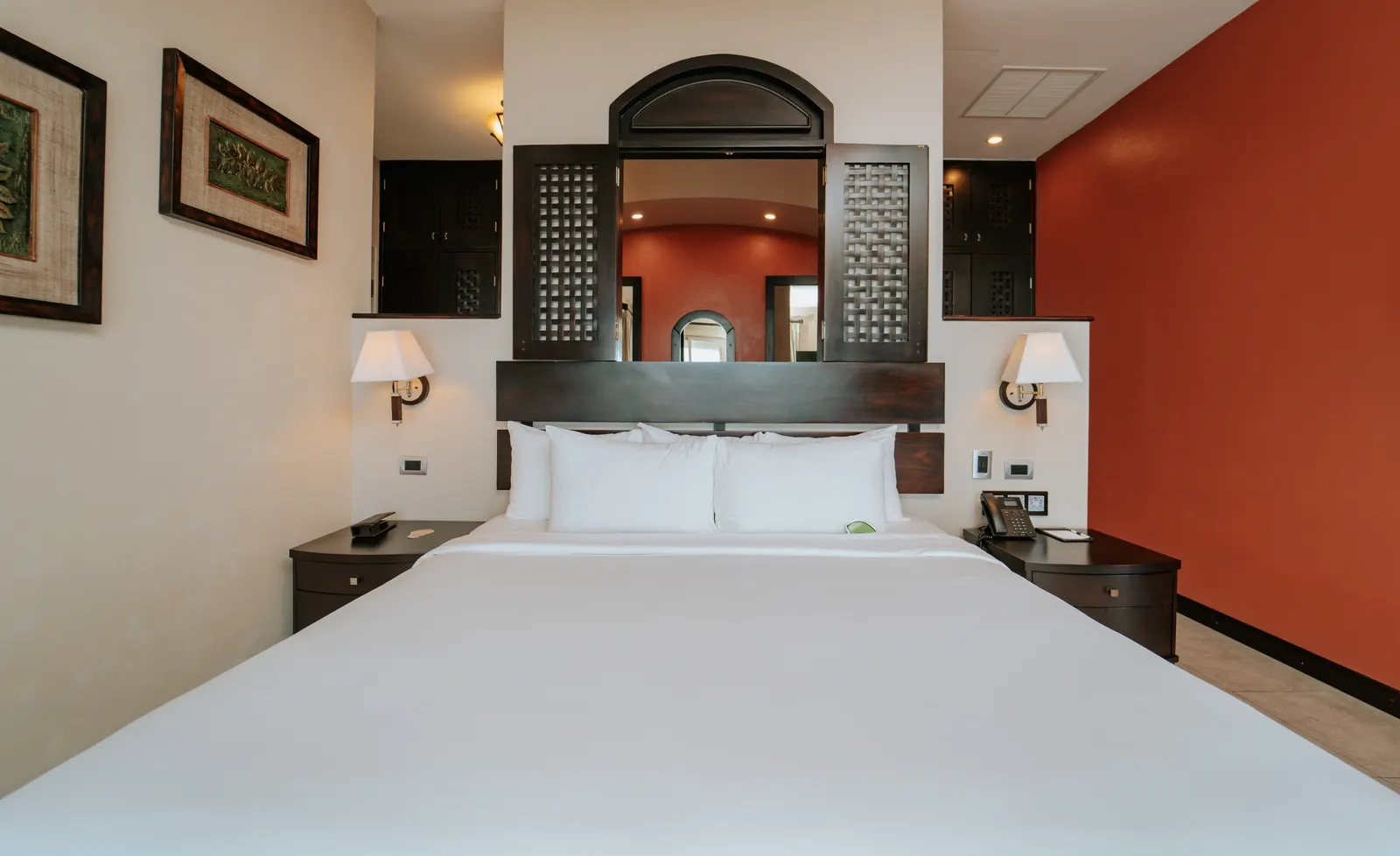 A king bed with a dark carved wood headboard and white linens in a hotel suite.