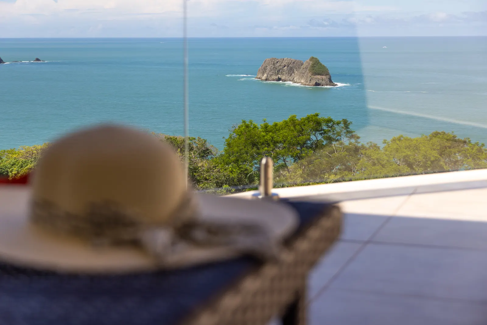 A straw sun hat rests in the foreground of a view toward a rocky sea stack and the open ocean.